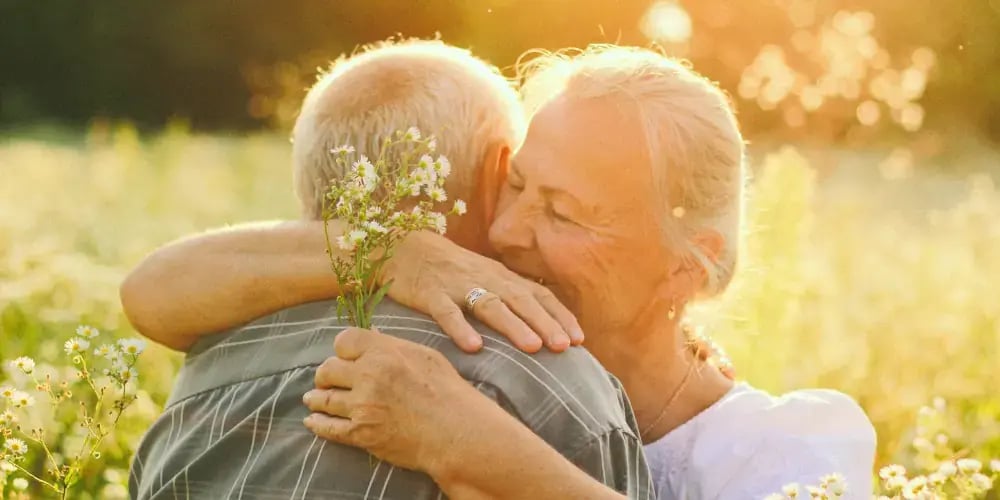 Senior couple embracing with wildflowers in hand, representing the emotional aspects of caring for elderly parents.