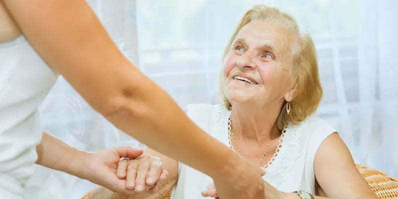 Carer offering support to a smiling elderly woman, illustrating the duty of care in aged care settings.