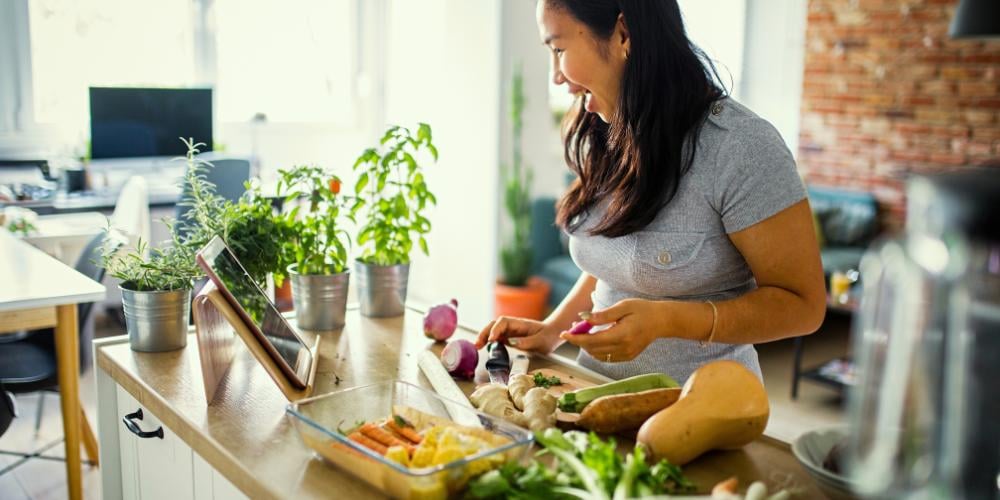 A caregiver joyfully preparing a nutritious meal in a bright kitchen, showcasing the meal preparation service included in a Level 3 Home Care Package.