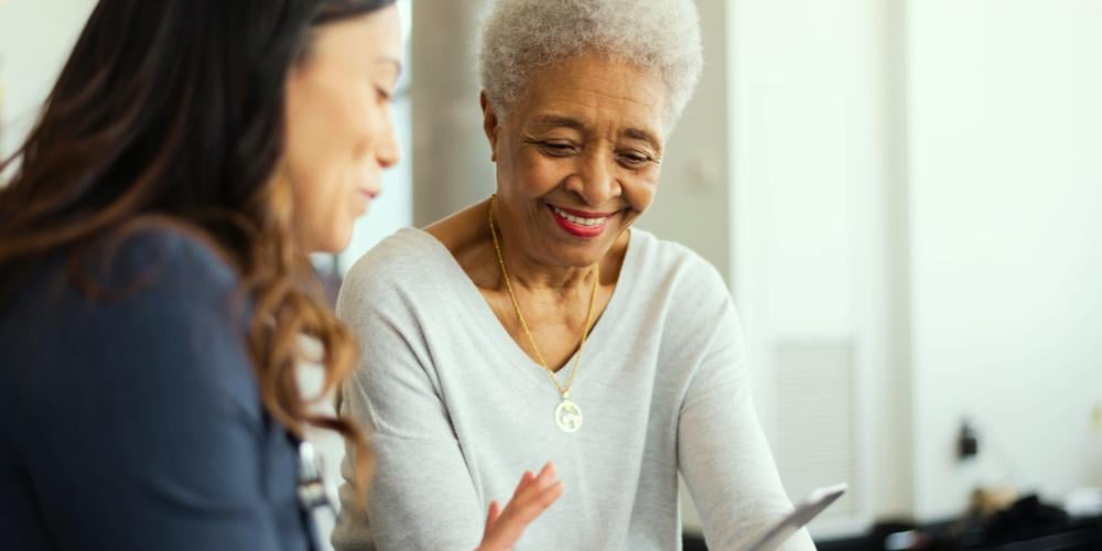 A compassionate home care worker discussing a Home Care Package Level 4 plan with an elderly woman, who is smiling and looking at paperwork.
