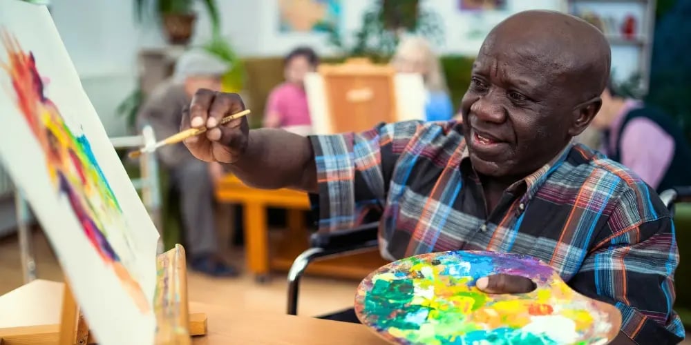 Older man in a wheelchair painting, demonstrating NDIS improved daily living through art activities.