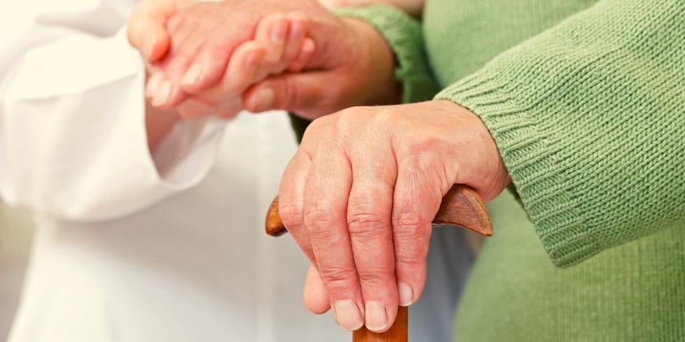 A carer holding hands with an elderly lady in need of supprt.