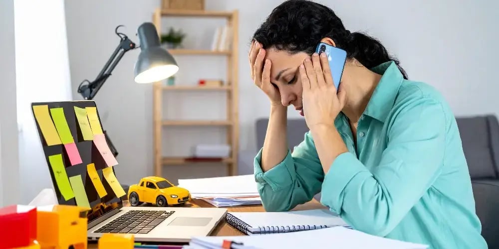 A family caregiver experiencing burnout, looking stressed while on the phone and trying to manage work and caregiving responsibilities from her desk.