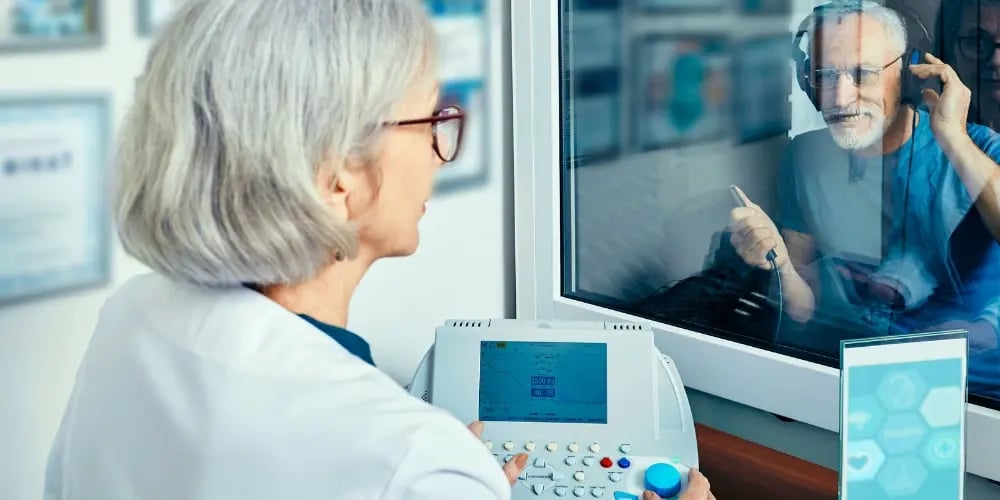 Audiologist conducting a hearing test (audiogram) on an elderly man in a soundproof room, diagnosing sensory hearing loss.