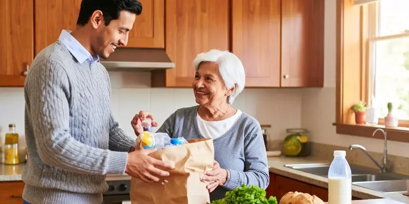 A friendly carer provides domestic assistance by helping an elderly woman unpack groceries in her kitchen, making daily life easier.