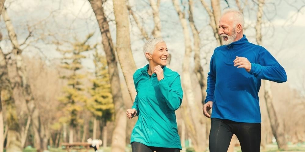 An elderly couple exercising (jogging in the park) which can help to prevent dementia.