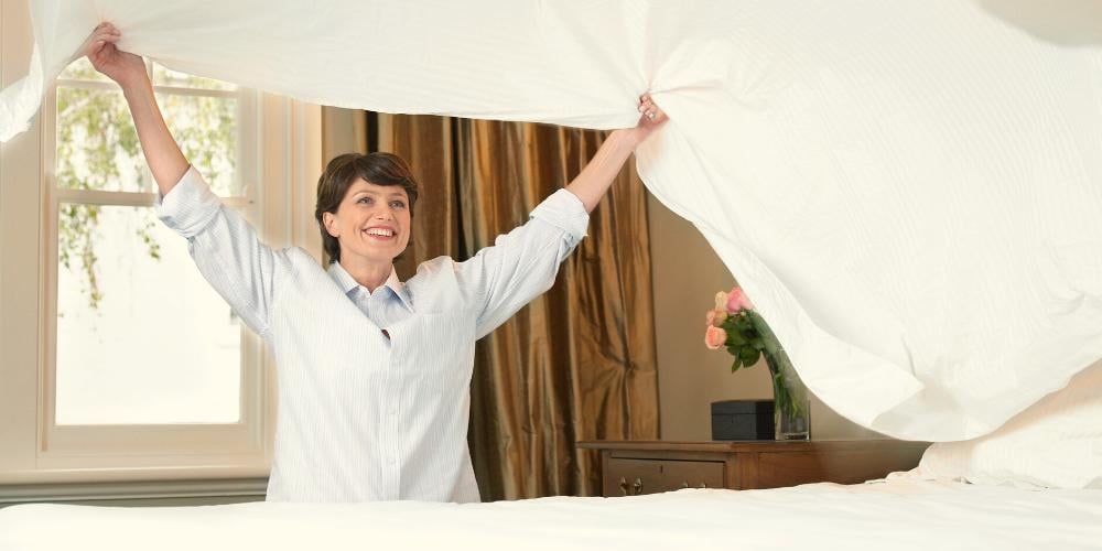 A cheerful care professional making the bed with fresh linens, reflecting the daily support provided in home care services to maintain a comfortable and clean living environment.