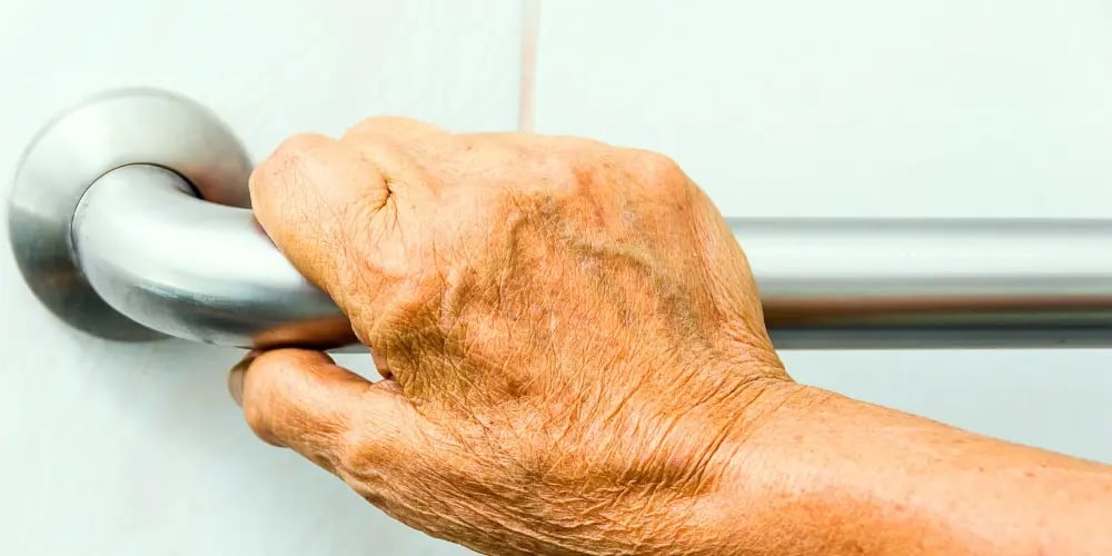 Close-up of an elderly hand gripping a safety grab bar, demonstrating fall prevention measures at home.