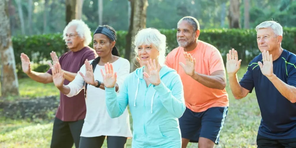 Group of seniors practising balance exercises outdoors, highlighting physical activity as a method for fall prevention in aged care.