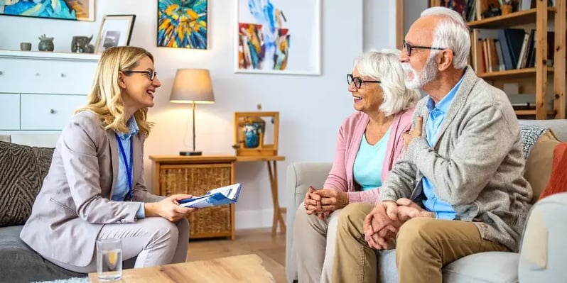 An in-home care provider has a friendly consultation with a senior couple in their home, discussing a care plan and building trust.