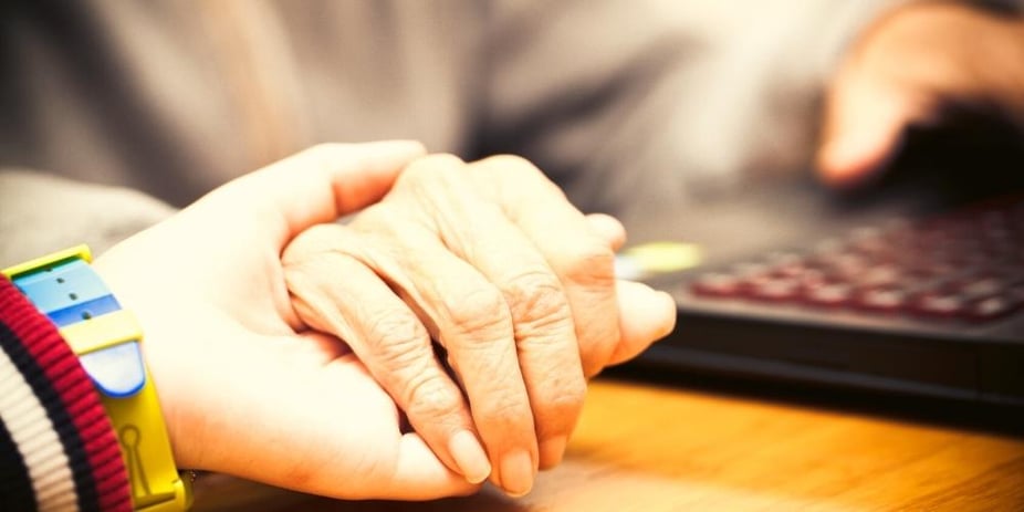 A Care For Family care professional holding hands to comfort a dementia patient.