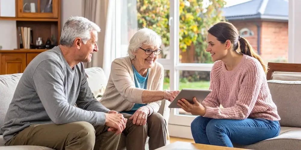 A senior couple actively participates in a consultation, reviewing their personalised in-home care plan on a tablet with a friendly care coordinator.