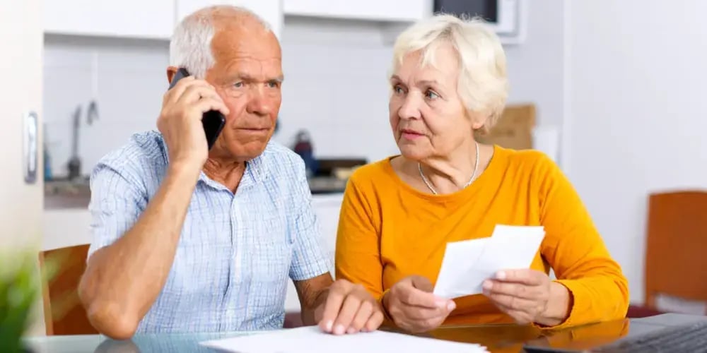 An elderly couple looks concerned while on the phone with My Aged Care, trying to understand the application process for government-funded in-home support.