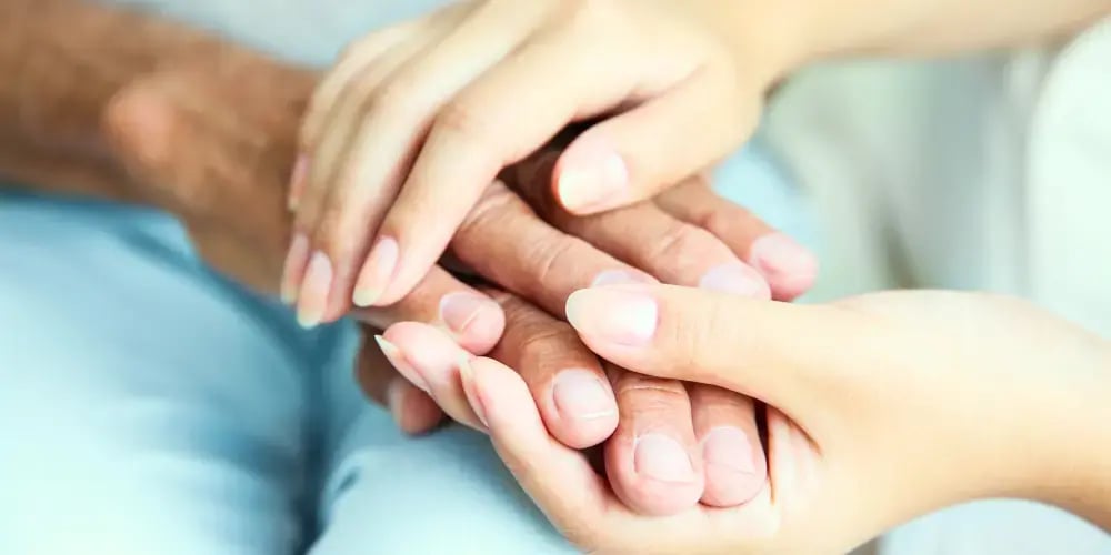 Close-up of two pairs of hands clasped together, symbolising support and compassion in high care aged care services.