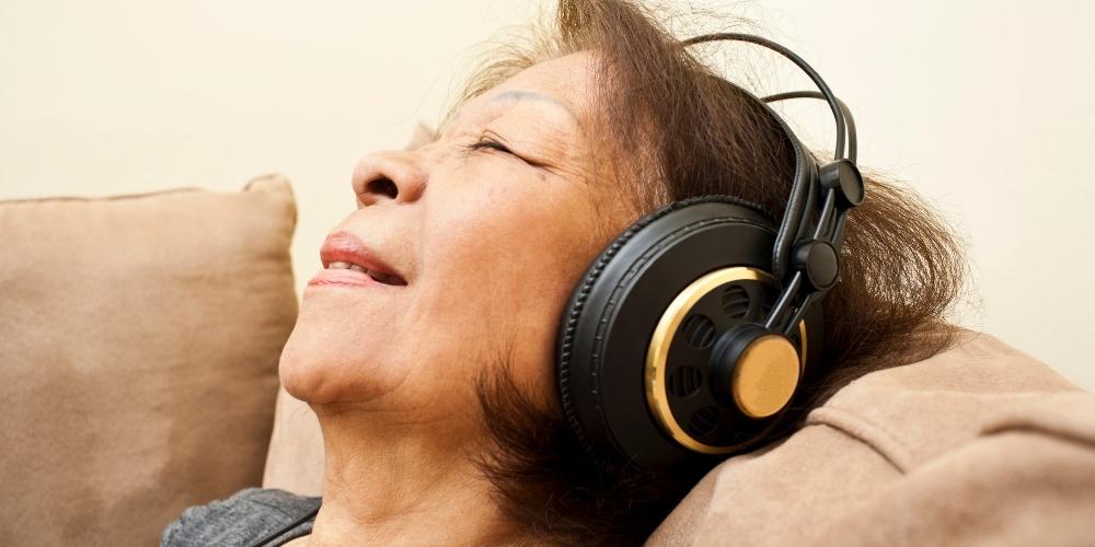 A lady with dementia wearing headphones and listening to relaxing music which is helpful when travelling.